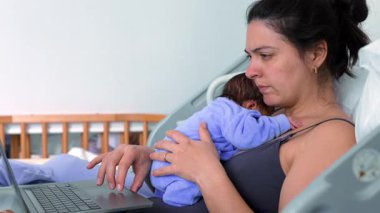Anne, dizüstü bilgisayarında çalışırken yeni doğmuş bebek tulumuyla hastane yatağında birden fazla iş yapıyor. Erken ebeveynliğin dengesini ve sorumlulukların sorumluluğunu gösteriyor.