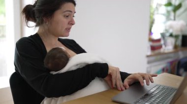 Anne, bebeğini kucağında tutarken aktif olarak laptopuyla meşgul oluyor. Kariyer ve çocuk yetiştirmenin modern zorluklarını gösteriyor. Kararlılığını ve bağlılığını yansıtıyor.