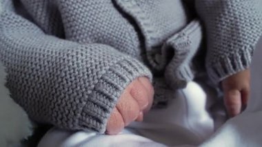 Örgü örülmüş bir süveterle kaplı yeni doğmuş bir bebeğin minik elleri, eski hayatın narin ve kırılgan doğasını ve rahat bir giysinin sıcaklığını vurguluyor.