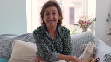 Sıcak, güneşli bir oturma odasındaki kanepede oturan yaşlı kadın. İçerik ifadesi ve dekoratif çevresi sıcak ve davetkar bir atmosfer yaratıyor.