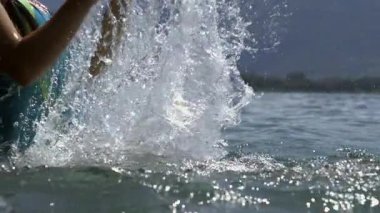 Küçük kızın göle su sıçrattığı kısmi görüntü, yüksek hızlı yavaş çekim yakalama, yaz eğlencesi, dinamik su hareketi, ferahlatıcı açık hava aktivitesi, eğlenceli enerji