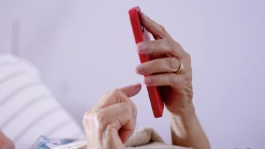 Üst düzey bir kadın yatakta, akıllı telefon kullanıyor, battaniyeyle örtülü, gözlüklü, rahat bir iç mekan ortamında, boş zamanlarını ve modern bağlantılarını yakalıyor.