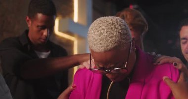 Latin kökenli, pembe ceketli Latin bir kadın. Bir dua anında omuzlarında destek elleri, inancı, duygusal gücü ve güveni ifade ediyor.