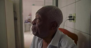 Afrika kökenli yaşlı bir adam fayanslı mutfakta yan yana oturuyor, konuşurken nazikçe gülümsüyor, samimi bir evde doğal etkileşim ve bağlantı kuruyor.