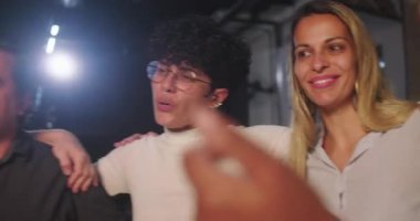 Birbirlerine yakın duran, kollarını birbirlerine dolamış bir grup insan sıcak, kapsayıcı ve destekleyici bir ortamda birlik, dostluk ve beraberlik anlarını paylaşıyorlar.