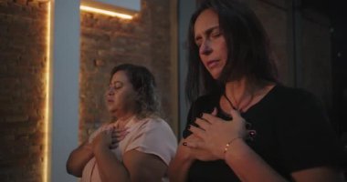 Hıristiyan kilise etkinliğine katılanlar, elleri göğsünde ve gözleri derin dualarla kapalı, arka planda parlayan haçla