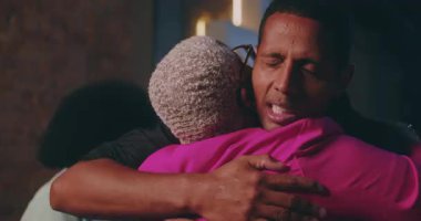 Kısa kıvırcık saçlı, gözleri kapalı, duygusal bir bağ ve güven anı paylaşan erkek, samimi bir grup toplantısında destekleyici arkadaşlarıyla ilgili ipuçları veriyor.