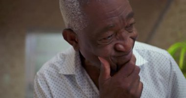 Yaşlı Afrikalı Amerikalı bir adam, çenesini dinlendirirken, düşünceli ve içsel bir tavırla endişe gösteriyor, kapalı alandaki hayat seçimlerini derin bir şekilde yansıtıyor.