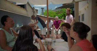 Aile verandada öğle yemeğinin keyfini çıkarıyor, çok nesilli grup sıcak, rahat bir ortamda sohbet, yemek ve kahkaha paylaşıyor, birlikteliği kutluyor.