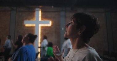 Gözleri kapalı bir kadın, kilisede dua ederken elleri sımsıkı bağlı, duygusal ibadet anı, Hristiyan inancı, Hristiyan maneviyatı, barış, ruhsal bağlantı