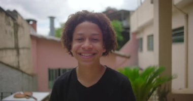 Latin Amerika yerleşim bölgesinde gülümseyen Afrikalı genç bir çocuk. Pembe ve bej duvarlar, fayanslı döşemeler, saksı bitkileri, neşeli bir ifade.