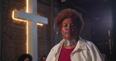 Afro-Amerikalı kadın aydınlanmış haçın, anlamlı bakışın, manevi bağlantının, kültürel ve inanç odaklı anın, güç ve gücün önünde kendinden emin bir şekilde duruyor.