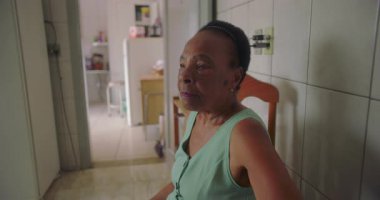 Afro-Amerikalı yaşlı bir kadının mutfakta yakın çekimi, düşünceli gözleri yalnızlığı ve yalnızlığı yansıtıyor, yaşlanma ve izolasyonun duygusal ağırlığını vurguluyor.
