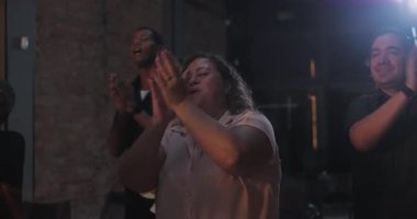 Toplu ibadet ortamında alkışlayan ve gülümseyen farklı bireylerden oluşan bir grup, sıcak bir mekanda parlayan bir haçın yanında toplandı.