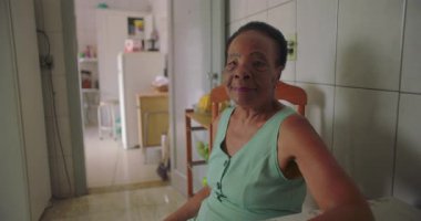 Rahat bir ev mutfağında yemek masasında oturan, düşünceli, bilgeliği ve yalnızlığı yansıtan yaşlı Afrikalı Amerikalı kadın, her gün huzurlu bir ortamda.