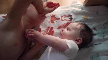 Küçük çocuk yatakta yatarken küçük kardeşine bakıyor. Yumuşak bir bağ anı, çocukluk bağı, aile sevgisi, kardeş ilişkisi, barışçıl ve sevecen bir ortam.
