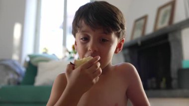 Küçük çocuk elmadan bir ısırık alıyor, yakın çekim, sıradan bir ev anı, taze meyvenin tadını çıkarıyor, sağlıklı atıştırmalıklar, çocukluk beslenmesi, rahatlatıcı atmosfer, doğal ifade.