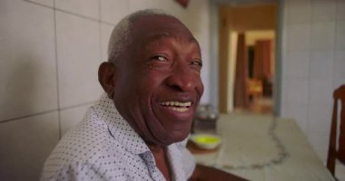Yemek masasında sıcacık gülümseyen yaşlı bir adam fayanslarla döşeli mutfağında rahat bir şekilde oturuyor, neşe ve neşe saçıyor, neşeli bir anı paylaşıyor.