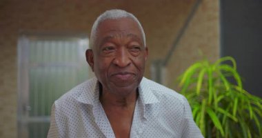 Yaşlı Afrikalı Amerikalı adam kameraya özgüvenle bakıyor, bilgelik ve duruş yayıyor, sakin ve ayakları yere basan bir kişiliği açık havada sergiliyor.
