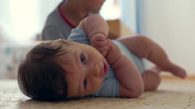 Bebek mindere uzanıyor, kameraya bakıyor, yumuşak yüz ifadesi, sıcak ev atmosferi, erken çocukluk gelişimi, sakin bir an, bebek merakı, barışçıl ev ortamları