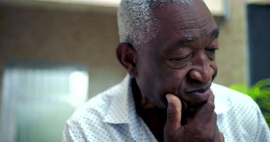 Yaşlı Afrikalı Amerikalı bir adam açık hava ortamında dalgın görünüyor.