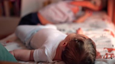 Bebek yatakta uzanıyor, rahat ve meraklı, nazik hareketler, çocukluk gelişimi, çevreyi gözlemleme, huzurlu bir yuva kurma, sakin bir durumda bebek.