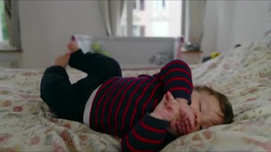 Bebek yatakta yan yana yatıyor. Oyuncak hareketlerle, küçük eller ve ayaklar hareket halinde. Rahat ve merak uyandıran bir yatak odası ve yumuşak bir yatak odası.