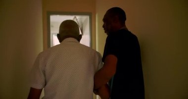 Yaşlı adam genç bir adamın yardımıyla yürüyor, ilgi ve destek anına dokunuyor, nesiller arasındaki empati ve bağlantıyı yansıtıyor.