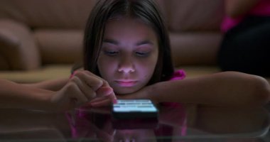 Parlak akıllı telefon ekranına odaklanırken kollarında dinlenen genç kız dijital bağlılık, teknoloji kullanımı ve modern çocukluk alışkanlıklarını gösteriyor