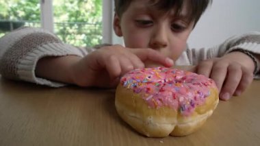 Oğlan, ahşap masaya renkli şekerlemeler serpiştirilmiş pembe bir donutu dürtüyor, çocukluk arzularını, hoşgörüsünü, merakını ve beklentilerini temsil ediyor.