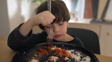 Domates soslu pilav yiyen, çatal tutan ve hevesle bir ısırık alan, çocukluktan kalma samimi bir yemek ve keyif anı sunan genç bir çocuk, yaşam tarzı için ideal.