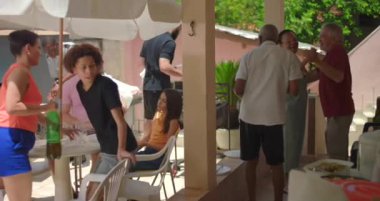 Çeşitli aile ve arkadaşlar açık havada yemek yiyip kaynaşıyor, sıcak bağlantıların ve günlük bir öğle yemeği sırasında hareketli bir atmosferin tadını çıkarıyorlar.