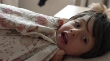 Genç çocuk çiçekli battaniyenin altında yatıyor, rahat bir sabah rutini, ev yatak odası, çocuk uyanma, aile zamanı, rahat bir başlangıç, rahat ve sıcak, sabah ışığı.