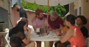 Yaşlı bir adam açık hava öğle yemeği sırasında bir grupla iletişim kuruyor. Rahat bir aile ortamında toplum ve eğlenceyi teşvik ediyor.