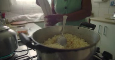 Yaşlı Afrikalı Amerikalı kadın sıcak suyu bir tencere pilavın içine dökerek geleneksel yemek pişirme, bakım ve adanmışlığın özünü yakalıyor sıcak ve samimi bir mutfak ortamında.