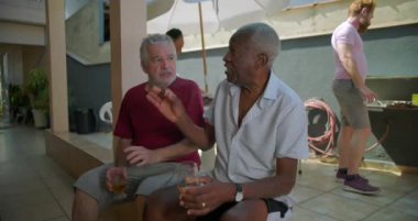 İki yaşlı adam, arka planda bir barbekü olayıyla rahatça oturup, sohbet ederek rahatlar ve dostça sohbet ederler.