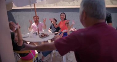 Bir aile barbekü partisinde coşkulu jestler düzenleyen ve alkışları yöneten yaşlı adam, eğlenceyi, bağlantıyı ve paylaşılan neşeli deneyimleri vurguluyor.