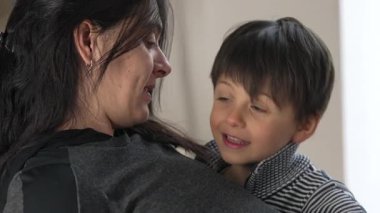 Anne ve çocuk samimi bir anı paylaşıyor, kapalı ortam, göz teması, aile bağı, sevgi ve şefkat, doğal ışık, barışçıl sahne, annelik bağı, ev ortamını besleme, sıcaklık
