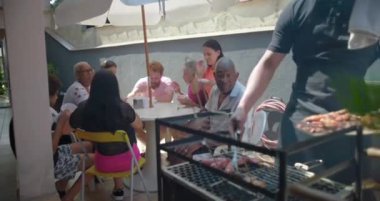 Arkadaşlar ve aile, ızgara yiyeceklerle barbekü toplantısının keyfini çıkarıyorlar. Açık hava ortamında paylaşılan yemeklerle çok kültürlü bir topluluğun bağ kurduğunu gösteriyorlar.