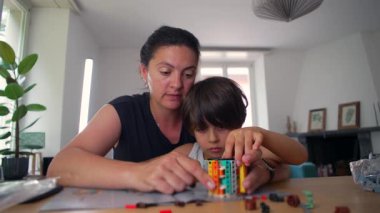 Anne, küçük oğluna bir bina etkinliğinde yardım ediyor. Her ikisi de ev ortamında işbirliği, öğrenme ve yaratıcılığı ön plana çıkarmaya odaklanıyor.