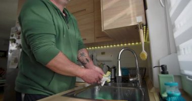 Adam mutfak lavabosunda bulaşıkları yıkıyor, iyi organize edilmiş modern mutfak ortamında temizlik ve ev işleri yapıyor.