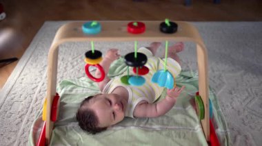 Bebek bir oyun hasırının üzerinde uzanıyor, renkli asılı oyuncakları gözlemliyor, duyusal keşiflere odaklanıyor ve erken çocukluk gelişimi ve ev ortamında oyun oynuyor.