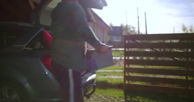 Adam kutu konteynırını araba bagajına koyup arka bahçeye kapatıyor, dış görevler veya ev geliştirme projesine hazırlanıyor, organizasyon ve paketlemeye odaklanıyor