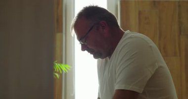 Banyo aynasının önünde düşünceli bir şekilde oturan adam, sakin bir ifadeyle yan profil görüntüsü, sessiz ve huzurlu iç mekan ortamını yansıtıyor.