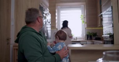 Baba bebeğini kucağında tutarken anne mutfakta hazırlanıyor sıcak ve sevgi dolu bir aile ortamında ev ortamında.