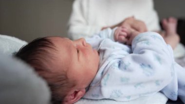 Yeni doğan bebek yukarı bakarken, büyükanne bebek bezi değişiminden sonra kıyafet giyer, hassas ve şefkatli bir an, aile bağları, sıcak ev ortamı, çok nesilli aşk
