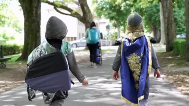 İki genç şövalye, yeni maceralara doğru giderken kostümleri akarken parkta birlikte yürürler. çocukluk hayalinin özü ve dostluk bağı neşeli bir ortamda.