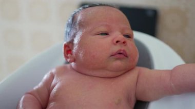 Küçük bir küvette yeni doğmuş bir bebek, ebeveynleri onları suda destekliyor, ıslak ciltlerinin, yüz ifadelerinin ve etkileşimlerinin detaylarını vurguluyor.