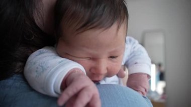Yeni doğmuş bebek, kolunda kabuğu soyulmuş bir anne babanın omzunda yatıyor. Bebeklik döneminin narin ve hassas anlarının yakın çekimini gösteriyor.