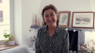Güzel dekore edilmiş bir ev ortamında mutluluk ve huzur duygusu gösteren, içten gülümseyen yaşlı bir kadının yakın çekimi.